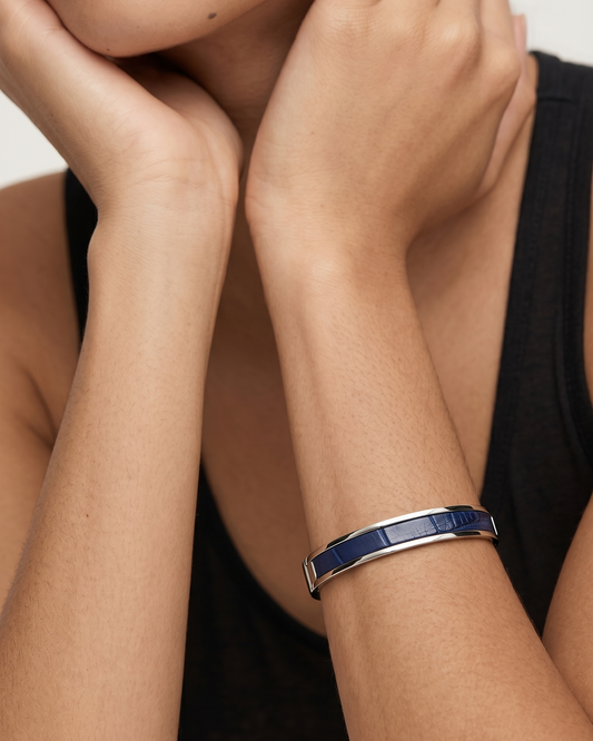 A Maverick Made. stainless steel leather cuff bracelet from Singapore, worn on the wrist in a clean minimalist portrait. The slim polished cuff features a deep blue leather inlay and reflective metal finish, styled with a black sleeveless outfit against a soft neutral backdrop. Natural skin tones, soft lighting and shallow depth of field create a refined editorial image for premium leather jewellery, artisan bracelets and handcrafted fashion accessories in Singapore.