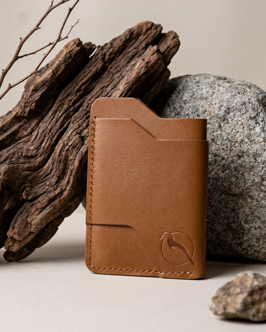 Handcrafted light brown leather card holder by Maverick Made. in Singapore, featuring hand stitching, an embossed hornbill logo, and a slim minimalist wallet design photographed on stone and driftwood.