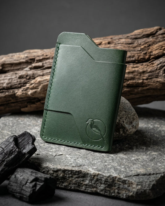 Handcrafted green leather card holder by Maverick Made. in Singapore, featuring hand stitching, an embossed hornbill logo, and a slim minimalist wallet design photographed on stone, driftwood and charcoal.