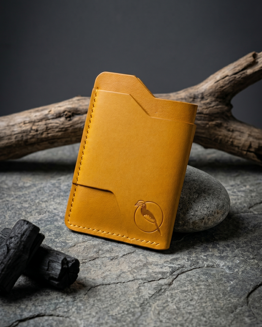 Handcrafted yellow leather card holder by Maverick Made. in Singapore, featuring hand stitching, an embossed hornbill logo, and a slim minimalist wallet design photographed on stone, driftwood and charcoal.