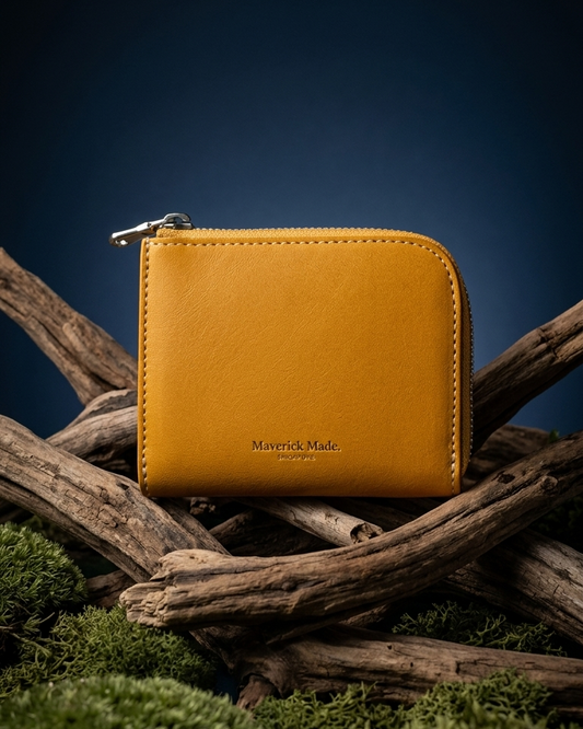 A yellow leather zip wallet by Maverick Made. Singapore, styled upright on layered driftwood with pale green moss and lichen in the foreground. The compact wallet features a rounded corner, visible zipper pull, contrast stitching and gold Maverick Made. Singapore logo stamping. A dark midnight blue gradient background and soft directional studio lighting create a rugged yet refined product photograph for premium leather goods, handcrafted wallets, artisan leather accessories and luxury carry in Singapore