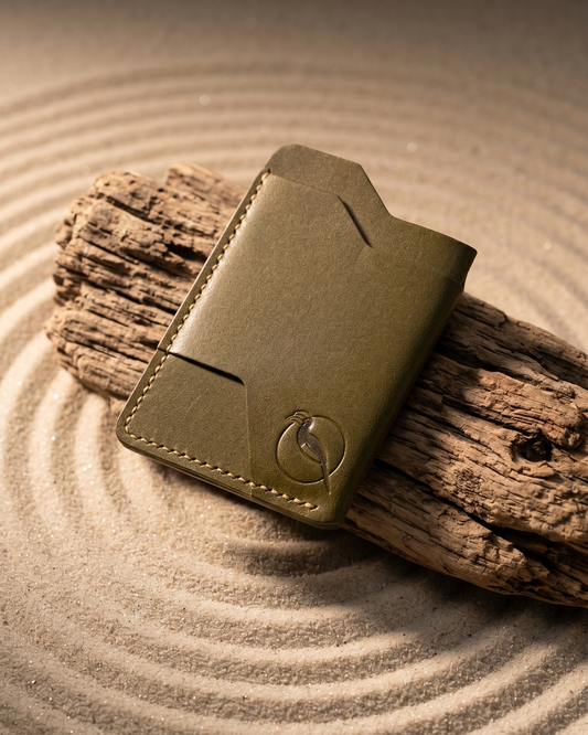 Handcrafted olive green leather card holder by Maverick Made. in Singapore, featuring hand stitching, an embossed hornbill logo, and a slim minimalist wallet design photographed on sand, driftwood and zen garden.