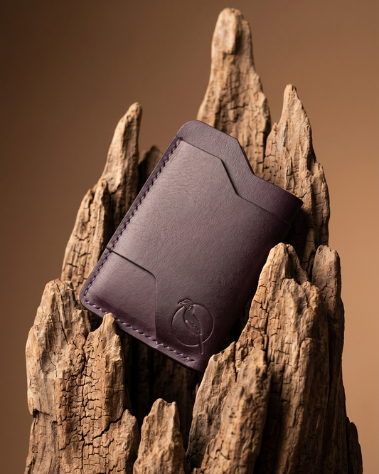 Handcrafted purple leather card holder by Maverick Made. in Singapore, featuring hand stitching, an embossed hornbill logo, and a slim minimalist wallet design photographed on driftwood.