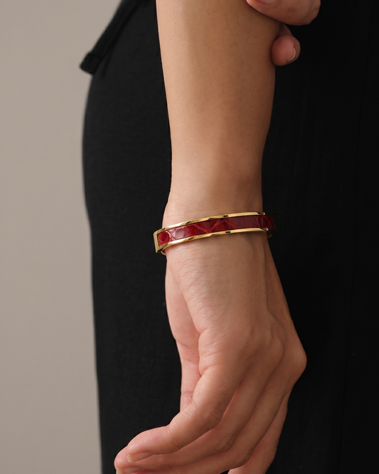 A Maverick Made. gold-tone stainless steel leather cuff bracelet from Singapore, featuring a deep red leather inlay with polished metal finishing. The bracelet is worn with a black minimalist outfit in a refined studio portrait with soft warm lighting and neutral tones. Clean composition and elegant styling create a luxury editorial image for premium leather jewellery, artisan bracelets and handcrafted fashion accessories in Singapore.