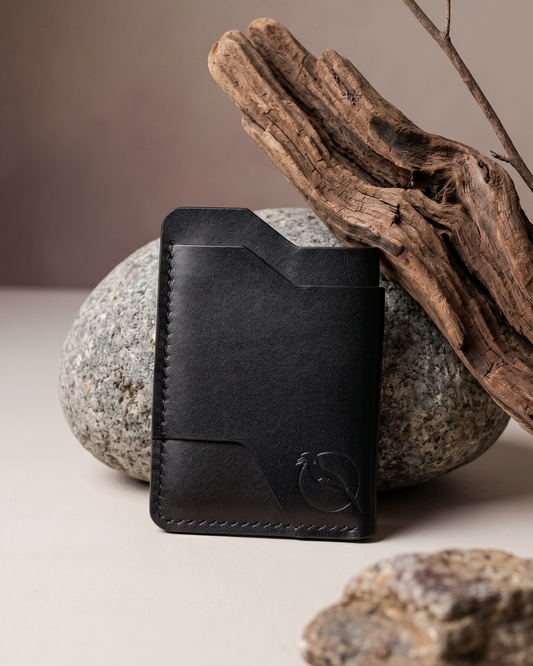 Handcrafted black leather card holder by Maverick Made. in Singapore, featuring hand stitching, an embossed hornbill logo, and a slim minimalist wallet design photographed on stone, driftwood and charcoal.