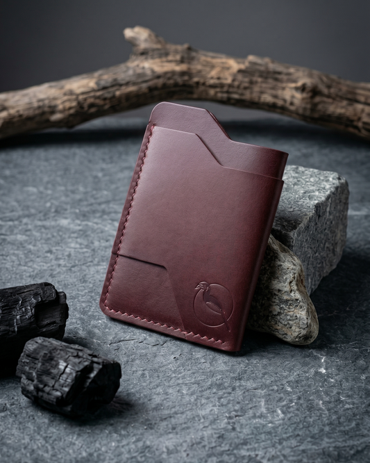 Handcrafted burgundy leather card holder by Maverick Made. in Singapore, featuring hand stitching, an embossed hornbill logo, and a slim minimalist wallet design photographed on stone, driftwood and charcoal.