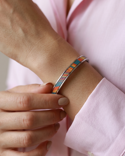 A Maverick Made. stainless steel leather cuff bracelet from Singapore, featuring a colourful striped leather inlay with warm orange, blue and red tones. The bracelet is worn with a white shirt in a soft minimalist portrait, with the wearer gently touching the cuff. Natural lighting, neutral styling and shallow depth of field create a refined editorial image for premium leather jewellery, artisan bracelets and handcrafted fashion accessories in Singapore.